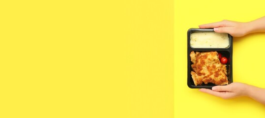 Hands holding container with healthy food on yellow background with space for text