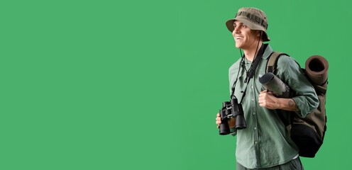 Male traveler with binoculars and backpack on green background with space for text