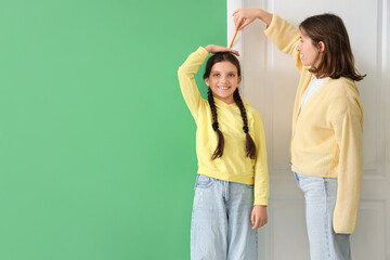 Cute girl with her mother measuring height at door near green wall