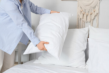 Young woman fluffing pillow on bed in bedroom, closeup