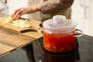 Young woman cutting onion for delicious borscht on wooden board in kitchen, closeup