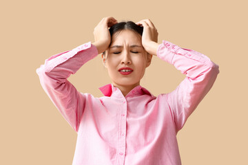 Young Asian woman suffering from headache on beige background. Brain Injury Awareness Month