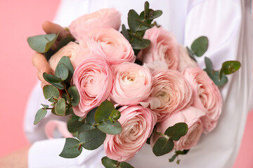 Young woman with bouquet of ranunculus flowers and eucalyptus on pink background, closeup