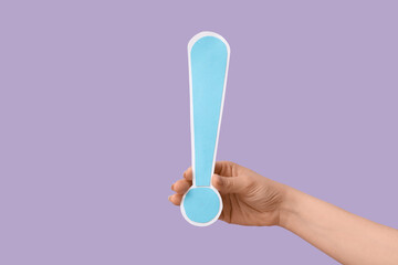 Female hand with paper exclamation mark against lilac background, closeup