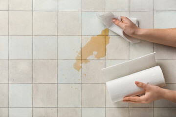 Woman wiping spilled coffee with paper napkins on white tile background