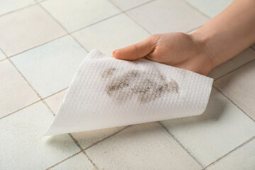 Woman wiping dust with paper napkin on white tile background
