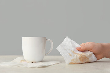 Woman wiping spilled coffee with paper napkins on white tile table near grey wall