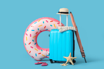 Suitcase with inflatable ring, beach umbrella and summer accessories on blue background. Vacation...