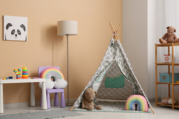 Interior of children's room with play tent, lamp, table and many toys in shelving unit near beige...