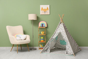 Interior of children's room with armchair, play tent, lamp and many toys in shelving unit near...