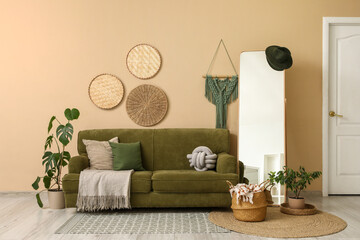 Interior of living room with green sofa, mirror, home decor and houseplants near beige wall