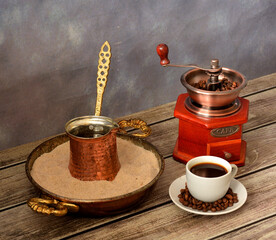 Cup of freshly brewed coffee on a saucer with beans, hand coffee grinder and tray with sand and...