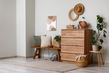 Interior of living room with wooden bench, hanging mirror, houseplants and home decor on commode...