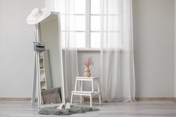 Interior of living room with mirror, stepladder and female accessories near window