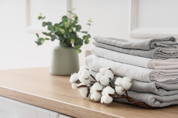 Stack of clean bed sheets with cotton flowers sprig on table in room
