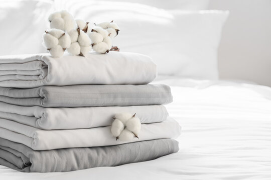 Stack of clean bed sheets with cotton flowers in bedroom