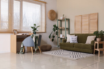 Interior of living room with sofa, shelving unit, workplace and stylish wooden blinds on window