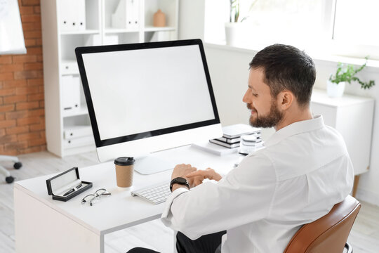Young businessman with blank computer checking smartwatch at table in office