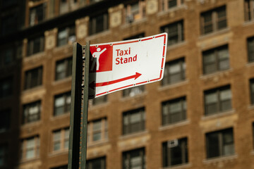 Urban taxi stand sign prominently displays pictogram of person and directional arrow. Bright daylight enhances informative and functional mood of city street setting.
