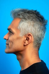 Obraz premium Visual idea of style for aging men. Blue solid background. A confident and happy man exuding charm. Elegant men's disconnected undercut haircut - midlife indian man with short hair.