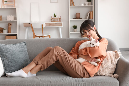 Beautiful young happy woman hugging her cute white cat on sofa at home