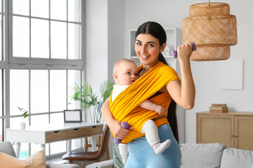 Sporty mother with her baby in sling and dumbbells training at home