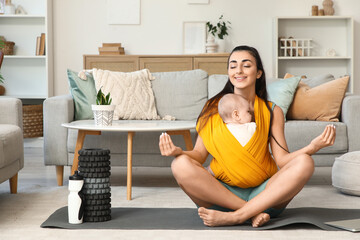 Sporty mother with her baby in sling meditating at home