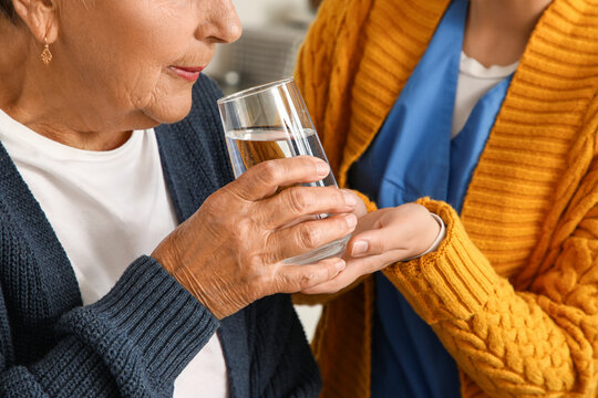 Fototapeta Senior woman drinking water with caregiver in kitchen, closeup
