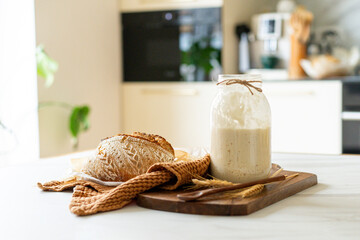 Crispy sourdough bread sits beside a glass jar filled with active starter, accompanied by a rustic...