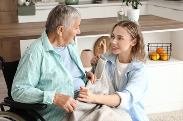 Young woman covering with plaid her grandmother in wheelchair at home