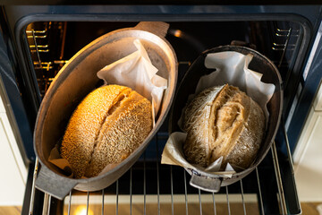 Two golden-brown loaves of bread rest in baking containers inside an oven, their crusts glistening...
