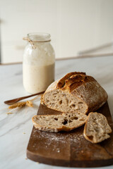 Crispy sourdough bread sits beside a glass jar filled with active starter, accompanied by a rustic...