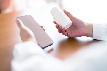 Doctor holding medicine bottle and smartphone, Telemedicine, online prescriptions, digital pharmacy services and remote consultation in modern healthcare and medical technology environments.