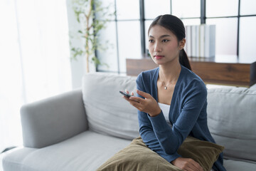 Asian woman Watching smart TV and using remote controller Hand holding television audio remote control at home with the remote control television