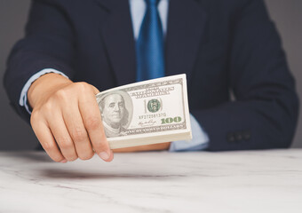 Businessman offering stack of hundred dollar bills at office table, concept of loan or payment.