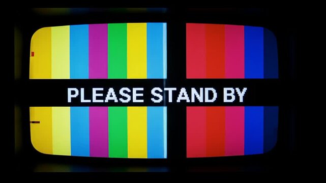 A vintage television screen displaying a colorful test pattern with "PLEASE STAND BY" message.