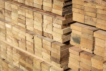 Stacked wooden planks in a lumberyard, showing various shades and textures of the wood, arranged in neat rows.