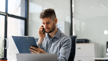 A smart Caucasian businessman sits confidently at desk in modern indoor office, using laptop for online consulting, showcasing professionalism, success, digital expertise in corporate environment.