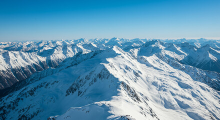 Majestic snow-covered mountains against a bright blue sky offering a stunning aerial view