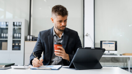 Fototapeta premium A smart Caucasian businessman sits confidently at desk in modern indoor office, using laptop for online consulting, showcasing professionalism, success, digital expertise in corporate environment.