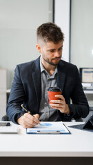 A smart Caucasian businessman sits confidently at desk in modern indoor office, using laptop for...