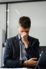 A stressed Caucasian businessman in a suit sit indoors at an office desk, suffering from office...
