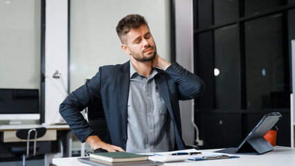 A stressed Caucasian businessman in a suit sit indoors at an office desk, suffering from office...
