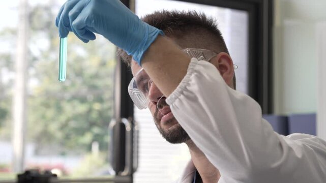Young Caucasian male scientist works in laboratory, analyzing chemical samples with glassware and microscope. research tools, experiments, data interpretation, pharmaceutical development.