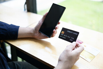 A man is holding a credit card and a cell phone. He is sitting at a table. Concept of modern life and the importance of technology in our daily lives
