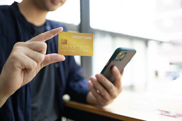 A man is holding a credit card and a cell phone. He is sitting at a table. Concept of modern life and the importance of technology in our daily lives
