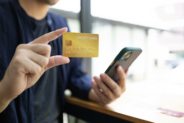 A man is holding a credit card and a cell phone. He is sitting at a table. Concept of modern life and the importance of technology in our daily lives
