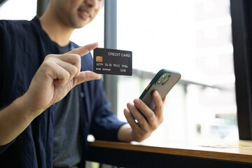 A man is holding a credit card and a cell phone. He is sitting at a table. Concept of modern life and the importance of technology in our daily lives
