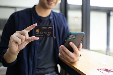 A man is holding a credit card and a cell phone. He is sitting at a table. Concept of modern life and the importance of technology in our daily lives
