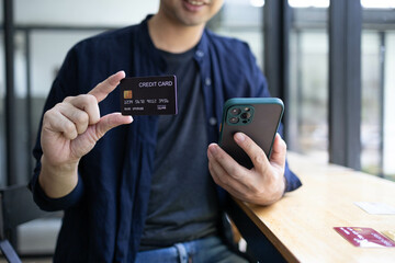 A man is holding a credit card and a cell phone. He is sitting at a table. Concept of modern life and the importance of technology in our daily lives
